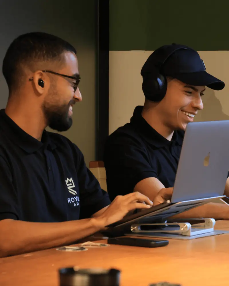 Dois membros do time Royal sorrindo enquanto trabalham no laptop
